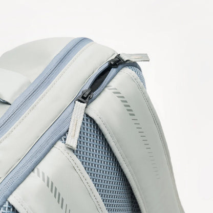 Close-up of the Kanso Intuko Tennis 23L Backpack in gray, featuring a mesh pocket, diagonal zipper, textured fabric, nylon straps, reflective print, and modern zipper pull. Its sleek design includes a handy racket compartment for added convenience.