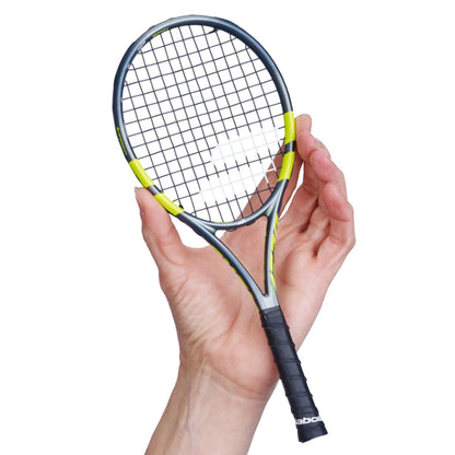 A hand holds a Babolat Mini Pure Aero 2026 Tennis Racket, featuring a black and yellow frame with a black grip, against a white background.
