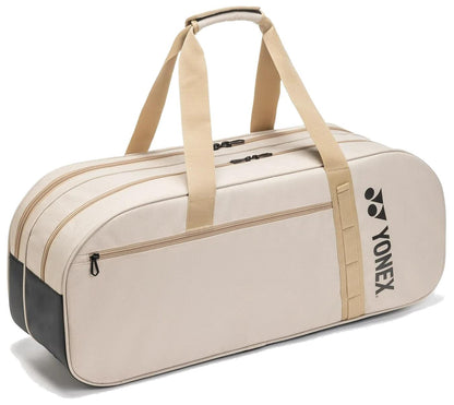 The Yonex BA72631WEX Gearlogic Tournament Tennis Bag in beige features tan straps, a front zip pocket, dual zippered main compartments, a padded handle, and a black Yonex logo on the side.