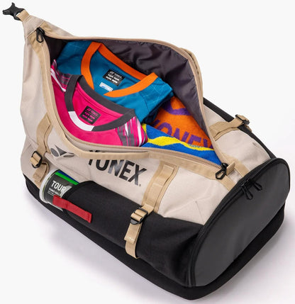 The Yonex BA72612EX Gearlogic Tennis Backpack in beige, ideal as a racket bag, is unzipped to show neatly packed sports shirts and a towel. It features handles, straps, and a "TOUR" label for easy carrying.
