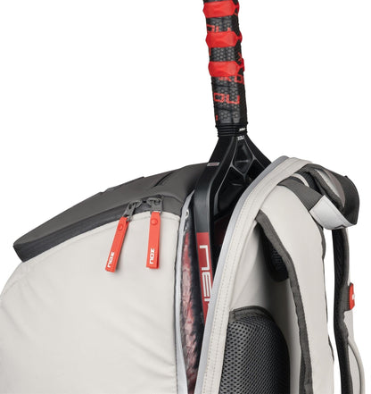 A close-up of the NOX Supra Pickleball Backpack - Cream by NOX, with black accents and red zipper pulls, ergonomic padded straps, and a tennis racquet with a red grip partially tucked into the side compartment.