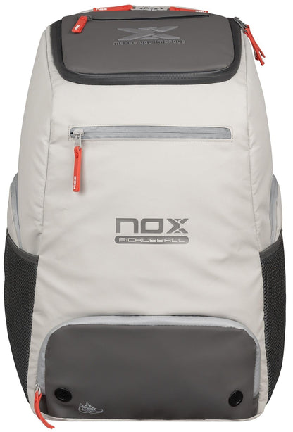 The NOX Supra Pickleball Backpack in cream features ergonomic padded straps, red zipper pulls, mesh side pockets, and a front compartment, displayed upright on a white background.
