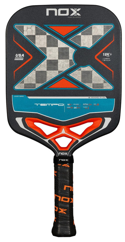 The NOX Luxury Tempo Pickleball Paddle features a black face with a gray and blue checkered "X" design, orange accents, and a NOX-branded grip on the black handle. Made from 18K aluminised carbon fibre for Exclusive Spin technology.