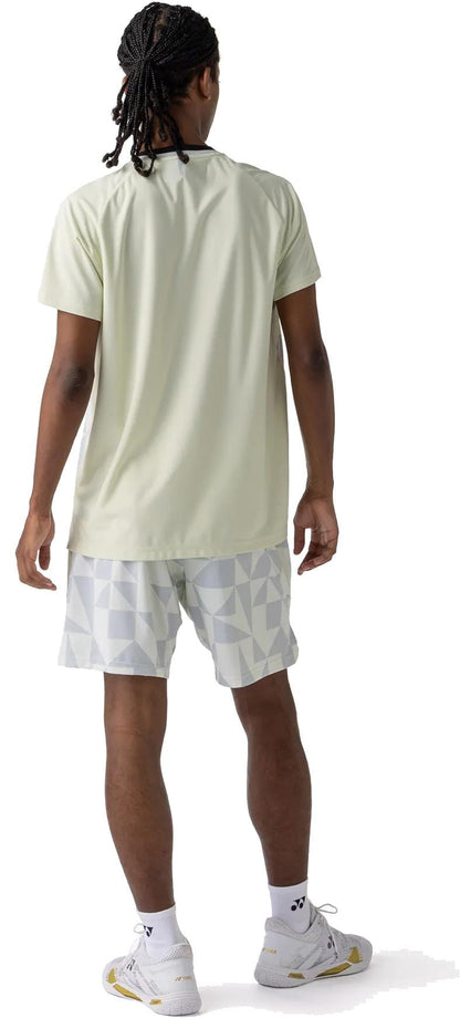 A person with braided hair faces away, wearing a light short-sleeve shirt, Yonex 15240YX Knit Mens Tennis Shorts in Champagne featuring a geometric pattern, white sports socks, and white sneakers against a plain white background.