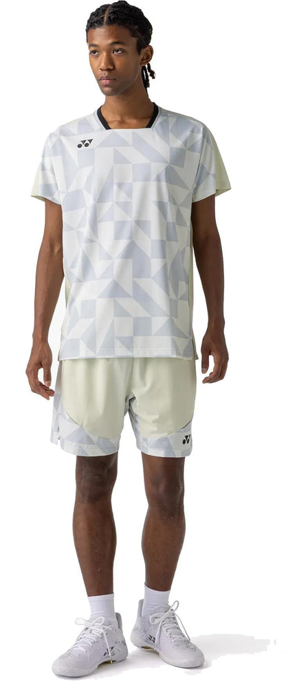 A person faces forward wearing a light geometric-patterned sports shirt and Yonex 15240YX Knit Mens Tennis Shorts in Champagne, paired with white socks and gray athletic shoes. The background is plain white.