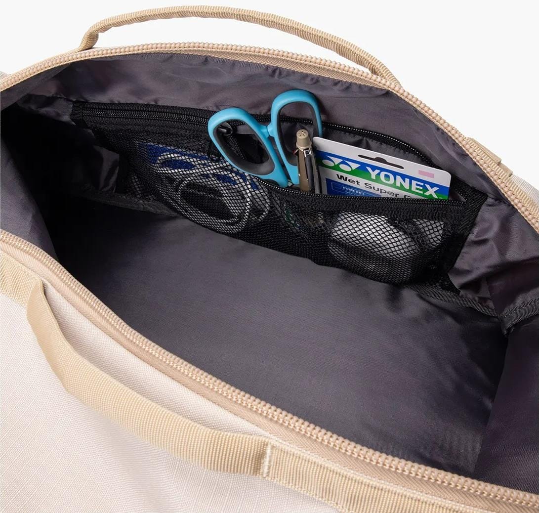 The Yonex BA72612EX Gearlogic Tennis Backpack in beige features a spacious main compartment, fabric handles, and an interior mesh pocket holding blue scissors, a key, and a Yonex wet super grip packet.