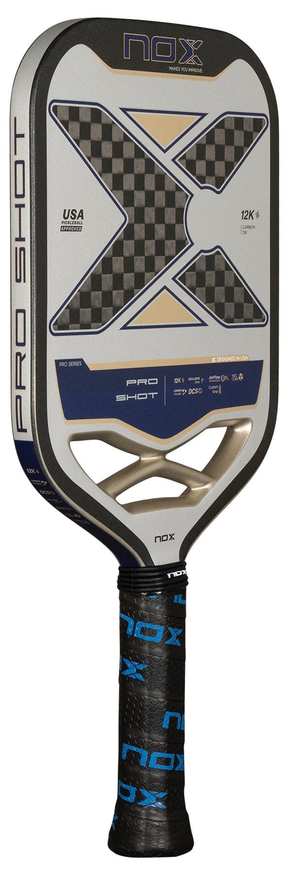 The NOX Pro Shot Pickleball Paddle by NOX features a large black and silver carbon fiber face with a checkered "X" design, a padded handle wrapped in black grip tape with blue "NOX" branding, and is labeled for professional use.