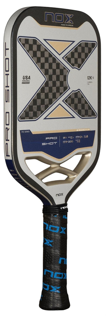 The NOX Pro Shot Pickleball Paddle by NOX features a large black and silver carbon fiber face with a checkered "X" design, a padded handle wrapped in black grip tape with blue "NOX" branding, and is labeled for professional use.