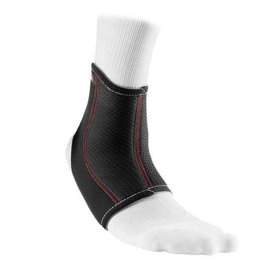 A white socked foot wears the McDavid Ankle Sleeve from McDavid, a black neoprene ankle support brace with red stitching. This ankle sleeve covers the ankle and extends partially up the calf, providing effective compression therapy and support.