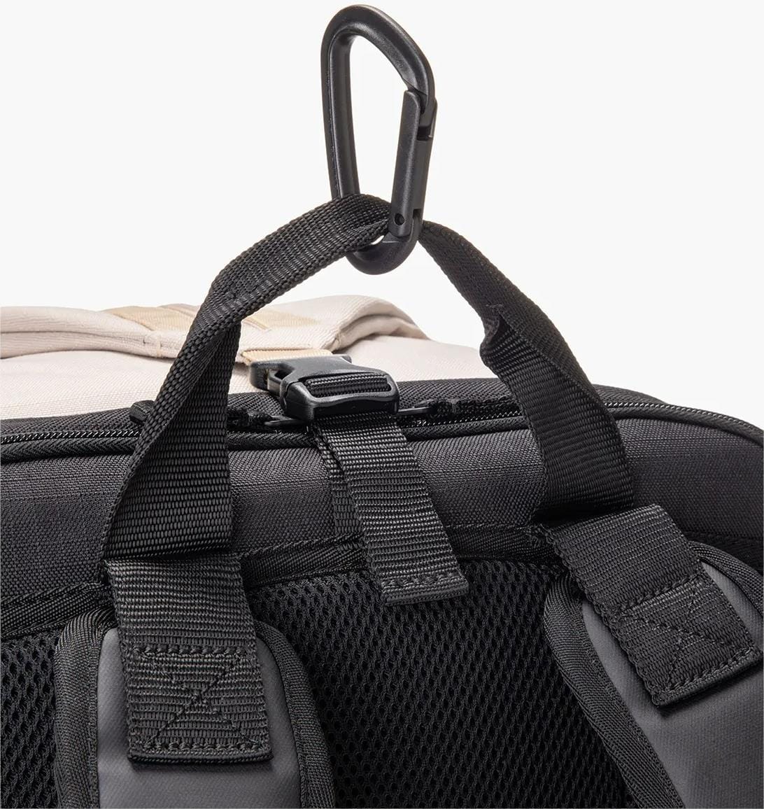 Close-up of Yonex BA72612EX Gearlogic Tennis Backpack in beige, showing its black straps, mesh back panel, and a plastic hook at the top handle for hanging or attaching items.