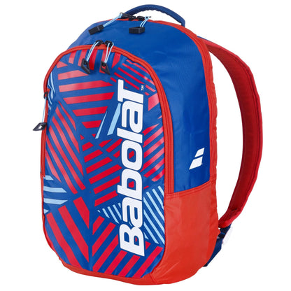 The Babolat Kids Tennis Backpack in blue and red features a geometric pattern with the brand name in large white letters. Designed for young athletes, it has a top handle, two shoulder straps, and a zippered compartment.