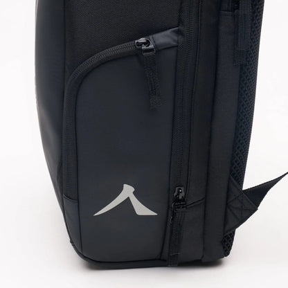 Meet the Kanso Intuko Tennis 23L Backpack in Black: featuring a sleek glossy panel with a minimalist gray arrow logo. Designed for everyday use, it has two visible zippers—a top horizontal and a side vertical—providing easy access to separate compartments for simple organization.