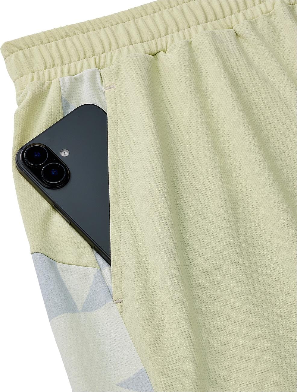 A black smartphone peeks out from the pocket of Yonex 15240YX Knit Men's Tennis Shorts in Champagne, featuring an elastic waistband, breathable knit fabric, and a geometric side pattern.