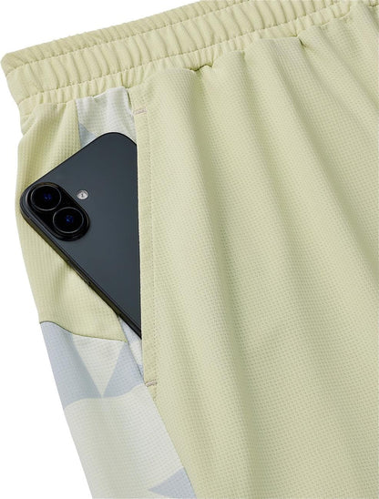 A black smartphone peeks out from the pocket of Yonex 15240YX Knit Men's Tennis Shorts in Champagne, featuring an elastic waistband, breathable knit fabric, and a geometric side pattern.