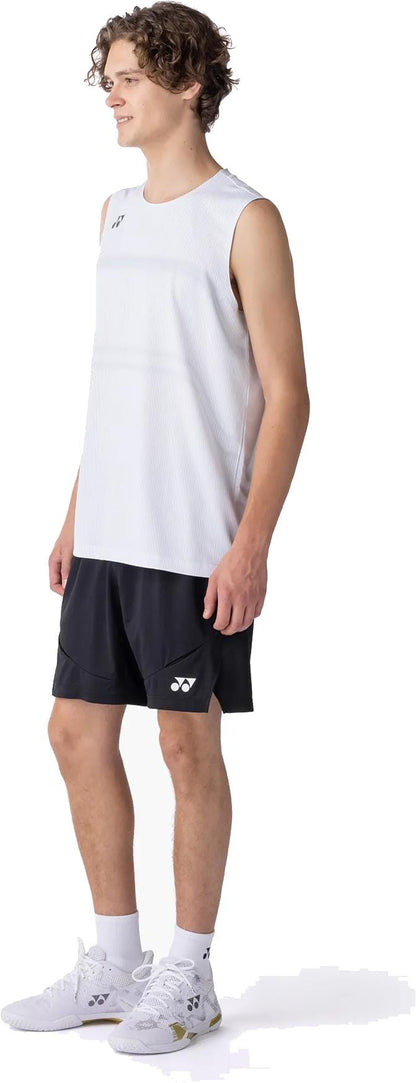 A young man stands smiling, wearing a sleeveless white sports shirt, Yonex 15239YX Knit Men's Tennis Shorts in black, white socks, and white athletic shoes. He faces slightly right against a plain white background. Brand: Yonex.