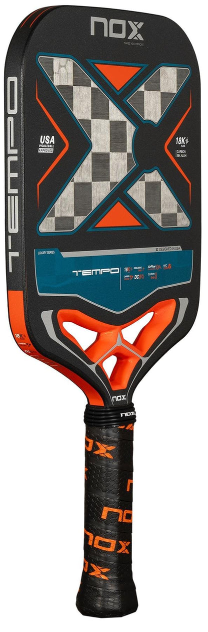 Close-up of the NOX Luxury Tempo Pickleball Paddle by NOX, displaying a black, orange, blue, and metallic silver 18K aluminised carbon fibre design and a textured handle with black grip tape featuring orange NOX logos.