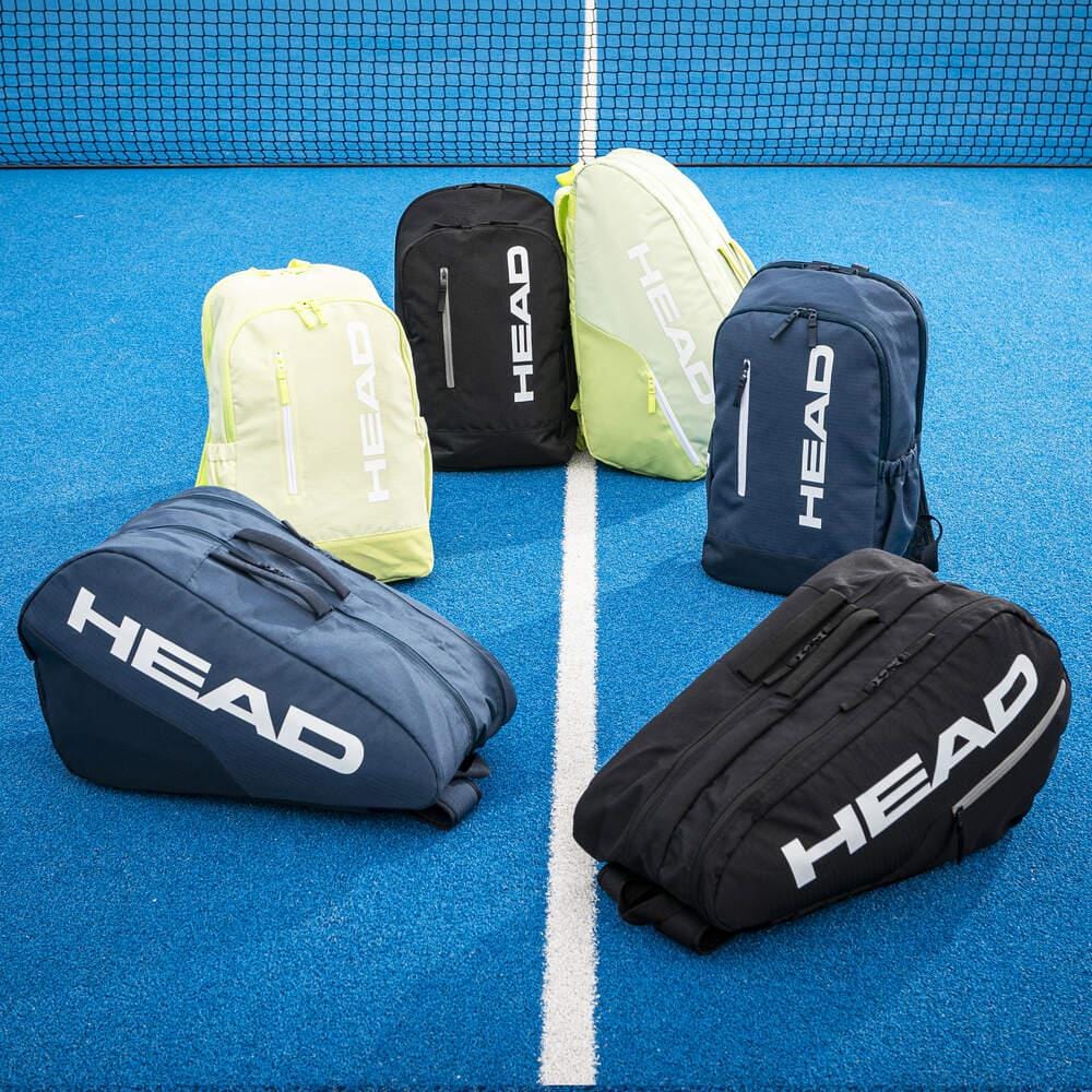 Six HEAD BASE Tennis Backpack 17L - Black bags are arranged on a bright blue court near the net—three upright and three lying down—all displaying the distinct HEAD logos.