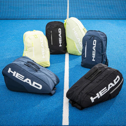 Six HEAD BASE Tennis Backpack 17L - Black bags are arranged on a bright blue court near the net—three upright and three lying down—all displaying the distinct HEAD logos.