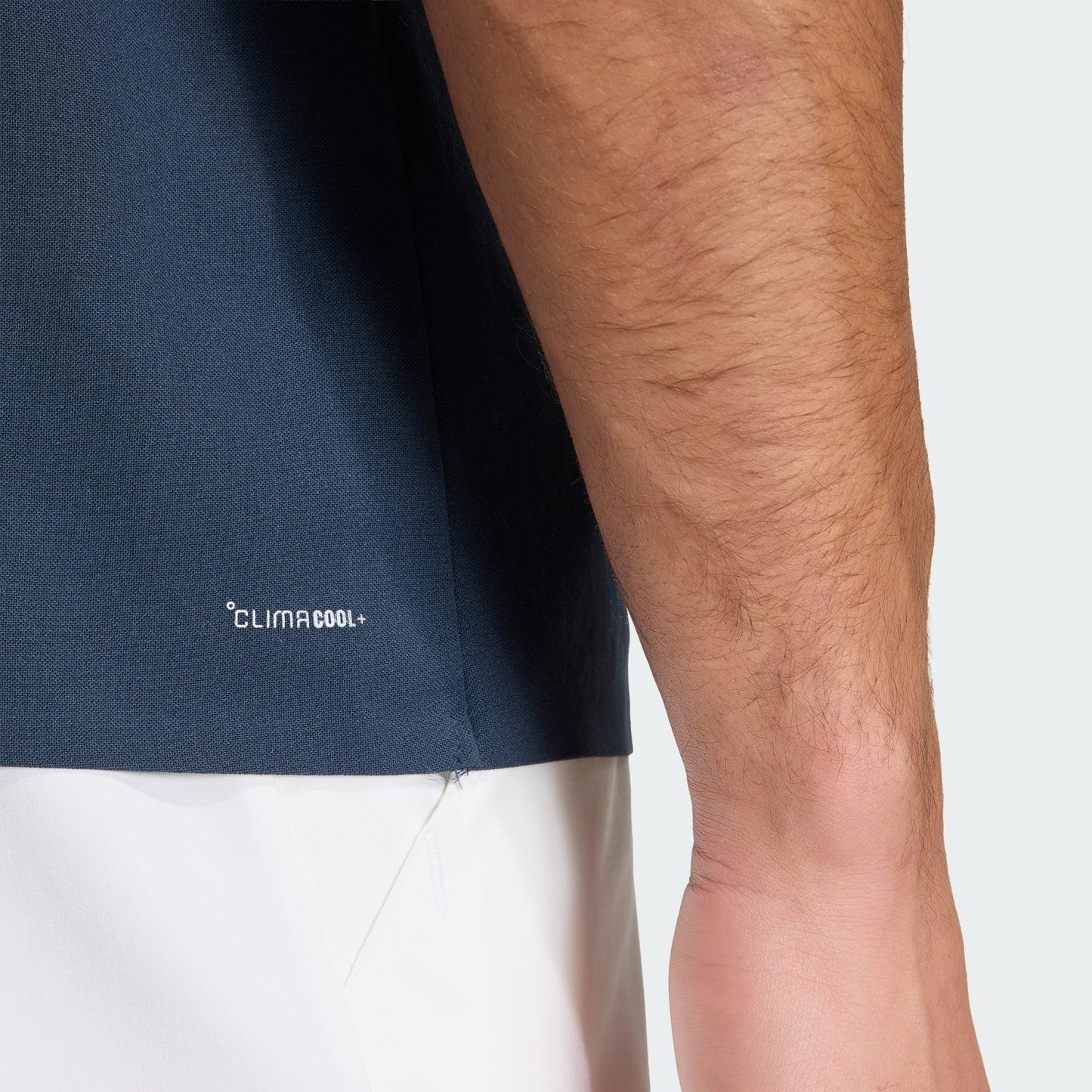 A close-up of a man's arm and torso wearing the adidas Climacool Men's Tennis Polo Shirt in Aurora Ink, highlighting its breathable fabric, FreeLift design, and detailed texture of the sleeve.
