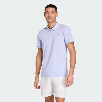 A man wearing an adidas Climacool Mens Tennis Polo Shirt in Violet Tone and white shorts stands against a plain light background, smiling at the camera.