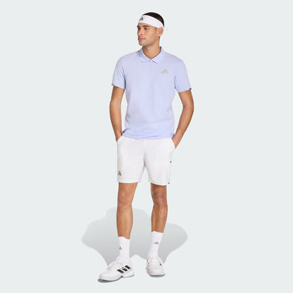 A person in an adidas Climacool Men's Tennis Polo Shirt (Violet Tone), white shorts, white sneakers, socks, and a white headband stands with hands in pockets against a plain light background.