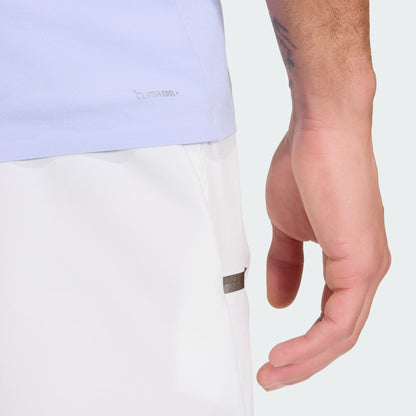 A close-up of a person's right hand resting on their thigh, wearing the adidas Climacool Mens Tennis Polo Shirt in Violet Tone and white shorts, with "CLIMACOOL" text visible and a forearm tattoo.