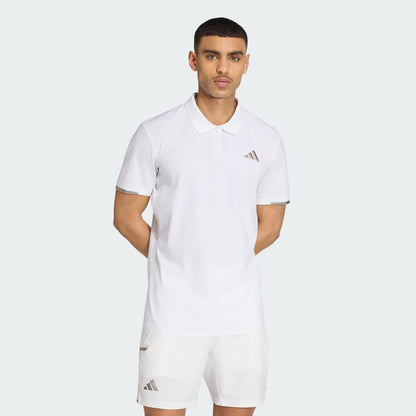 A man stands with his hands behind his back against a light gray background, wearing an adidas Climacool Mens Tennis Polo Shirt in white and matching shorts, both featuring the adidas logo.