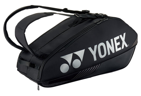 The Yonex 92426EX Pro 6 Racket Tennis Bag in black, adorned with a white logo, includes two shoulder straps and offers multiple zippered compartments, featuring a dedicated shoe compartment. It is crafted to efficiently carry up to six rackets along with other sports equipment.