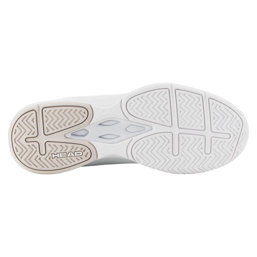 The image displays the sole of the white HEAD Revolt Court Women's 2025 Tennis Shoes, featuring a zigzag and herringbone tread with "HEAD" on the heel. It includes translucent hexagonal details for lightweight comfort.