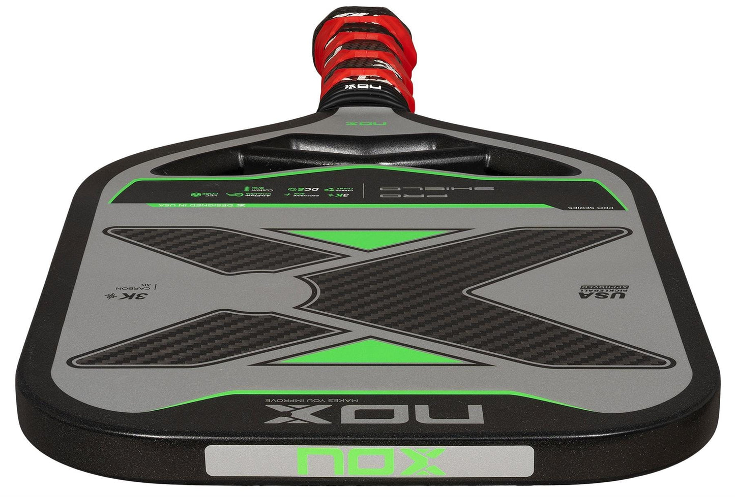 A close-up of the NOX Pro Shield Pickleball Paddle by NOX, with a black, gray, and green design, textured surface for spin, red and black grip, and "USA Pickleball Approved" on its carbon fiber face.