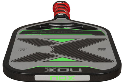 A close-up of the NOX Pro Shield Pickleball Paddle by NOX, with a black, gray, and green design, textured surface for spin, red and black grip, and "USA Pickleball Approved" on its carbon fiber face.