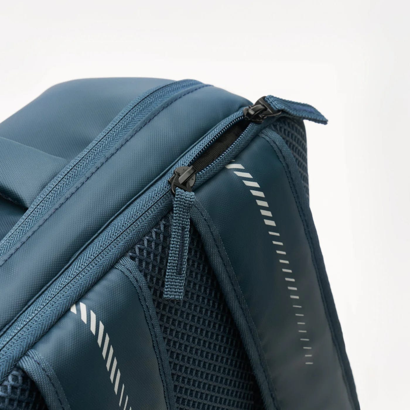 A close-up of the Kanso Intuko Tennis 23L Backpack - Navy with a partially open zipper reveals its sophisticated design. The navy material boasts a subtle sheen, reflective diagonal stripes, and a mesh panel for ventilation or extra storage—making it the perfect everyday companion.