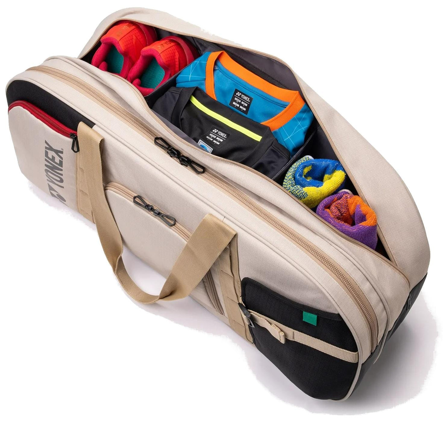 The Yonex BA72631WEX Gearlogic Tournament Tennis Bag in beige, from Yonex, holds red athletic shoes, folded blue and black shirts, plus rolled blue and yellow towels—organized perfectly for your next tournament.