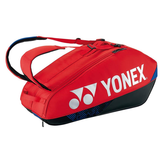 The Yonex 92426EX 6 Racket Pro Tennis Bag - Scarlet features a striking design with its scarlet fabric and dual shoulder straps, prominently displaying the classic Yonex logo in white on the side. Enhanced with black and blue accents at the base, this elegant tennis bag perfectly combines style with practicality for every tennis enthusiast.