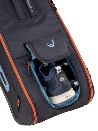 A close-up of the HEAD Pro 9 Racket Tennis Bag L - Navy by HEAD, featuring orange zippers and an open compartment with blue and white athletic shoes partially visible inside.
