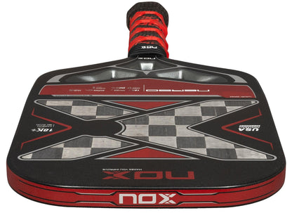 The NOX Luxury Nerbo Pickleball Paddle features bold black and red carbon fibre, a large "X" design with a checkered center, and NOX branding on the face and handle. Its handle is finished with stylish black and red grip tape.